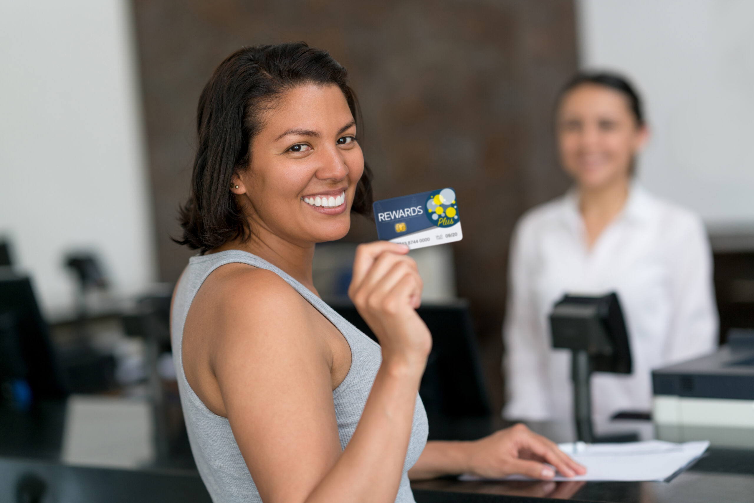 Beautiful woman on vacation checking in and holding a loyalty rewards card looking at camera smiling